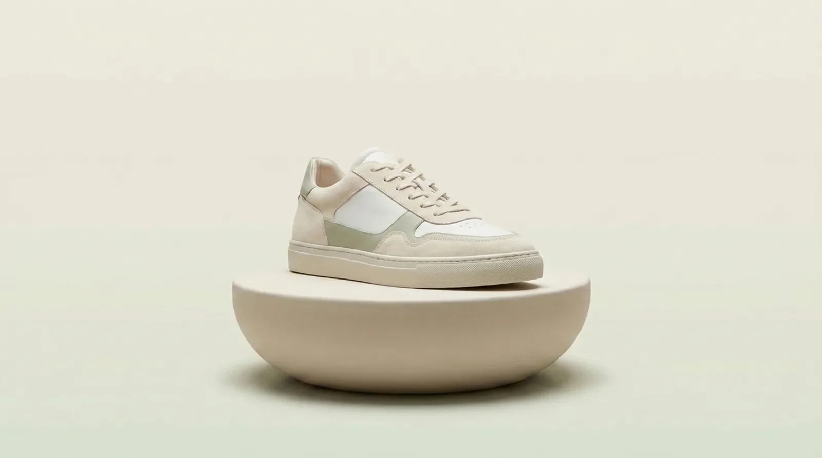 A cream and sage sneaker on a round plinth, the frame a 360 spin turns through